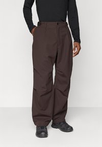 Brown wide-leg trousers with a front button closure, side pockets, and a smooth texture, paired with black shoes.