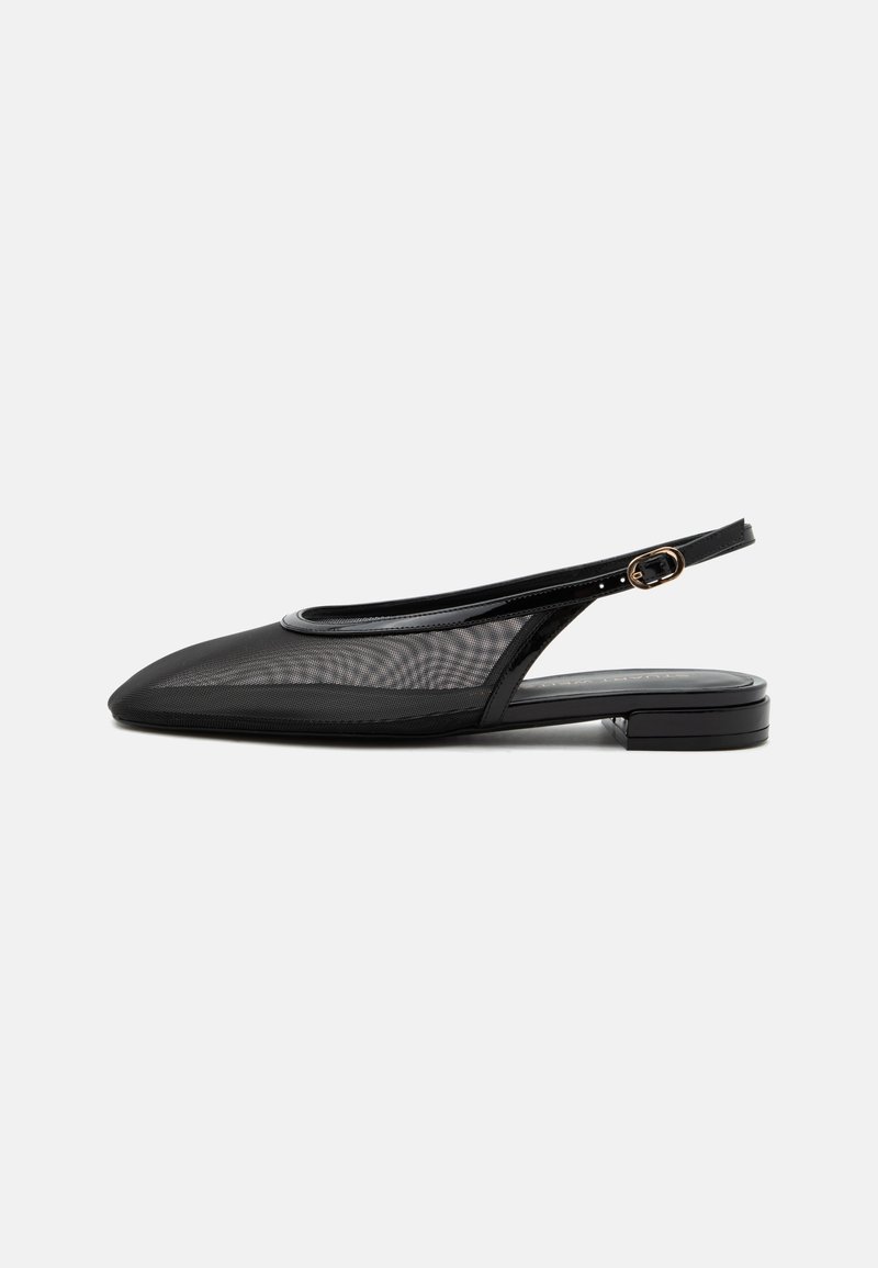 Chaussure plate noire à bride arrière, bout pointu, tige en mesh, bride à boucle réglable et petit talon empilé sur fond blanc.