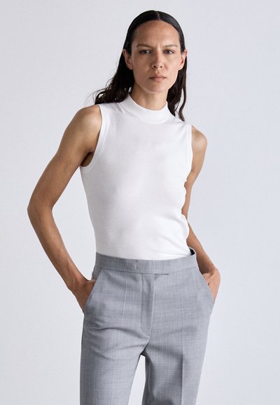 Top branco sem mangas com um decote alto, combinado com calças cinza claro sob medida com bolsos laterais e uma textura subtil.