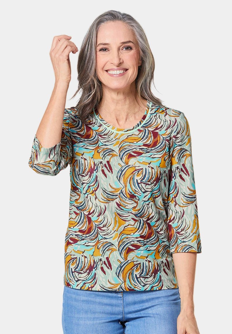 Multikleurige pullover met een draaiend patroon van teal, mosterd, bordeauxrood en crème. Gemaakt van zachte stof met driekwartmouwen.