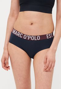 Mornarsko plave pamučne gaćice s širokim burgundskim elastičnim pojasom na kojem je srebrnim slovima ispisano "MARC O'POLO EST." Glatka tekstura, nisko rezanje.