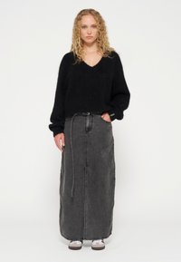 Suéter negro de lana con escote en V, combinado con una falda larga de mezclilla gris que presenta una abertura lateral y un cinturón de tela, llevada con zapatillas blancas.