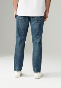 Jeans albastru din denim cu o croială slim-fit, având buzunare la spate și tiv desfăcut. Asortați cu pantofi sport albi și un tricou alb simplu.