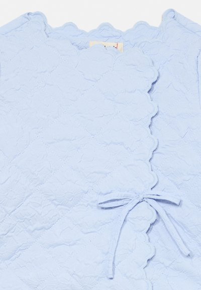 Material quiltat albastru deschis cu margini ondulate, cusături florale și un detaliu de fundă legată pe un articol vestimentar.