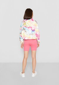 Kapuzenpullover met een multikleurig marmerpatroon, gecombineerd met roze shorts. Het model draagt witte sneakers en toont een casual outfit.