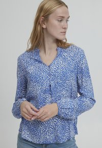 Blusa azzurra a manica lunga con bottoni frontali e un motivo a pois bianchi. Tessuto leggero con una vestibilità comoda e maniche con polsini.