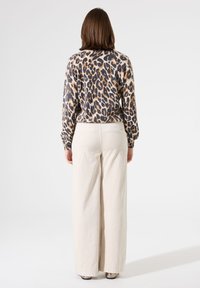 Pull en imprimé léopard à manches longues, associé à un pantalon large beige. Texture douce, palette de couleurs neutres, sans matériel visible.