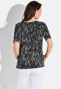 Haut à manches courtes noir et gris à motifs, avec un col rond et une coupe légèrement ajustée. Surface texturée et ourlet incurvé.