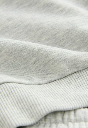 Tissu de sweat-shirt gris clair avec une surface lisse et un ourlet côtelé. Présente un tissage doux et texturé avec des variations subtiles de ton.