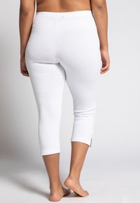 Leggings capri bianchi con una texture morbida, dotati di una vita elasticizzata e spacchetti all'orlo per un tocco aggiuntivo. Senza branding visibile.