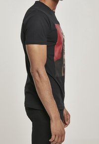 Svart bomullströja med korta ärmar, med en framsidesgrafik i röd och svart, rund hals och en standard passform.