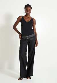 Top negro sin mangas con tirantes decorativos, combinado con pantalones anchos negros y un cinturón grueso negro con una hebilla de doble anillo dorada.