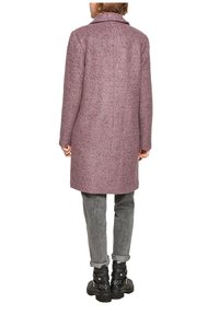 Lungo cappotto di lana rosa con una finitura testurizzata, colletto a revers e tasche laterali, indossato sopra jeans grigi e stivaletti neri con borchie.