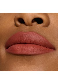 Rossetto opaco in una calda tonalità terracotta su labbra piene con un aspetto texturizzato, su uno sfondo di pelle liscia.