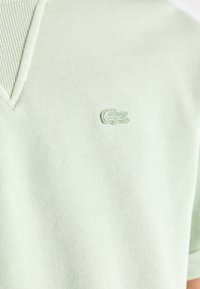 Light green polo shirt with a textured ribbed collar and a small embroidered crocodile logo on the chest. Soft, knitted fabric.
