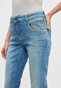 Φωτεινό γαλάζιο τζιν με στενή γραμμή, με διακοσμητική ραφή κατά μήκος των άκρων των τσεπών και κλασικό σχεδιασμό με πέντε τσέπες.