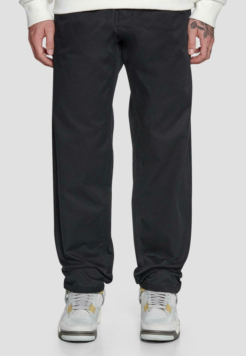 Schwarze Baumwollhosen mit geradem Bein, ausgestattet mit Seitentaschen und einer glatten Textur, kombiniert mit grauen und gelben Sneakers.