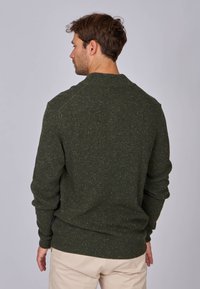 Pull en maille texturée de couleur vert foncé, avec un col rond et des poignets côtelés. La vue de dos révèle une coupe ajustée et un design minimal.