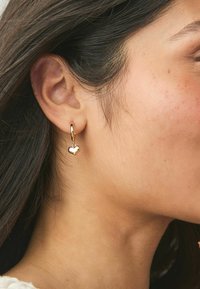 Orecchini a forma di cuore placcati in oro appesi a un cerchio, con una finitura liscia e lucida e una piccola chiusura per una vestibilità sicura.