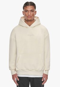 Cremfarbener Hoodie mit einer Vordertasche, oversized Passform und gerippten Bündchen. Verfügt über ein dezentes gesticktes Logo auf der Brust.