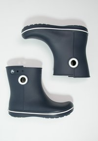 Bottes de pluie en caoutchouc de couleur bleu marine foncé avec des accents blancs, découpes circulaires, semelle texturée et finition lisse. Présente un bout arrondi et un petit talon.