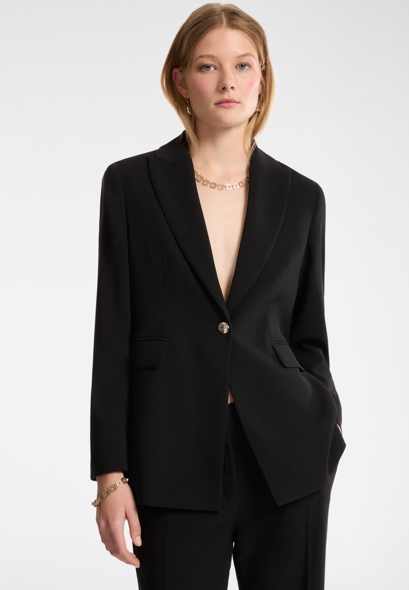 Blazer negro con cierre de un solo botón, solapas muescas y dos bolsillos frontales. Tela suave con un ajuste estructurado.