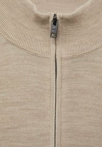 Beige zippered sweater with ribbed collar and cuffs. Features a smooth texture and a metallic zipper along the center front.
