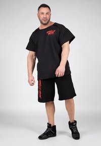 Black waffle-textured short-sleeve shirt with red "Gorilla Wear" logo paired with black shorts featuring matching logo. Black high-top shoes.
