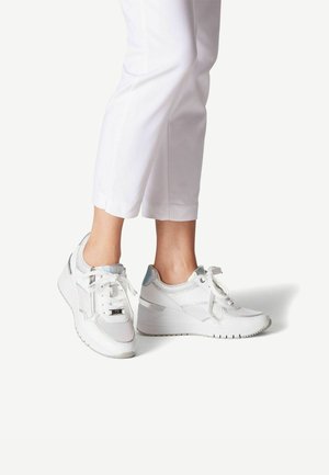 Baskets blanches avec une tige en maille, accents argentés et lacets plats. Équipées d'un talon compensé et d'une semelle texturée pour l'adhérence. Portées avec un pantalon blanc cropped.