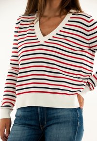 Pull à col en V avec des rayures horizontales rouges, bleu marine et blanches. Tissu tricoté avec une coupe décontractée et des poignets et un ourlet côtelés.