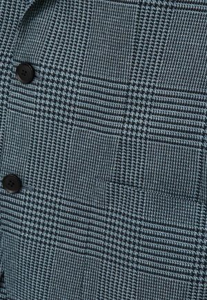 Tejido texturizado en azul oscuro con un patrón de cuadros, que presenta cuadrados claros contrastantes y botones negros. Detalle de tejido sutil en todo el material.