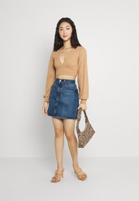 Top crop canelado bege com mangas longas, combinado com uma saia mini de ganga azul, sapatos de salto nude e uma bolsa estampada. Estilo simples e moderno.