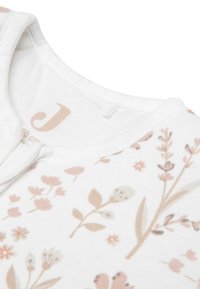 Tissu blanc avec des motifs floraux dans des tons de rose doux et de beige ; présente un col rond et un petit bouton-pression sur l'épaule pour un habillage facile.