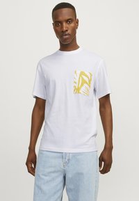 Hvid bomulds t-shirt med en gul mønstret brystlomme, korte ærmer og rund halsudskæring. Stoffet virker blødt og glat.