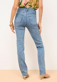 Džínové kalhoty s vysokým pasem v modré barvě se rovný fit, s dvěma zadními kapsami a jemným blednutím, spárovány s květinovým topem a tělovými lodičkami.