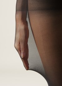 Czarne przezroczyste rajstopy o gładkiej fakturze; zbliżenie na rękę trzymającą materiał w okolicy uda. Miękki, lekki materiał.