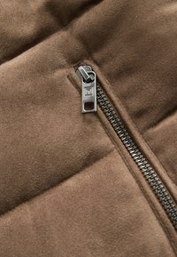 Smeđi kvadrantni materijal s mekom teksturom i srebrnim metalnim zatvaračem sa strane, koji sadrži detaljno šivanje i elegantan dizajn.