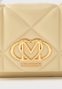 Μπεζ καπιτονέ τσάντα χειρός από ψεύτικο δέρμα με χρυσή καρδιά και λογότυπο, με λεία υφή και γεωμετρικό μοτίβο.