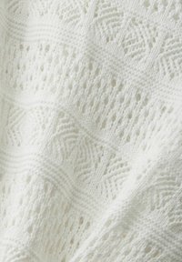 Weißer gestrickter Stoff mit einem strukturierten, offenen Muster, das diagonale Linien und geometrische Formen aufweist. Weich, leicht und luftig im Aussehen.