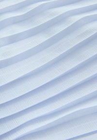 Pehme valge kangas, millel on ühtlaselt paigutatud horisontaalsed voltid, luues pinnale tekstuurse, lainelise mustri.