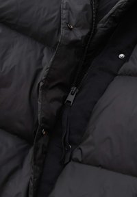 Zwarte gewatteerde jas met een gladde, glanzende buitenkant, rits sluiting, drukknoopjes en een gevoerde binnenkant die zichtbaar is bij de opening.