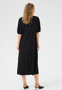 Black long dress with short puff sleeves, textured fabric, side slits, and a relaxed fit. Worn with black pointed-toe heels.