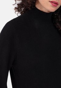 Pull noir en maille à col roulé avec un col ajusté et une texture lisse. Présente un col et des épaules côtelés.