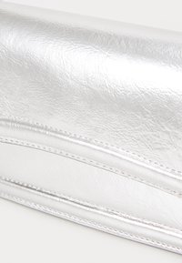 Stříbrná metalická psaníčko s texturovaným povrchem, zdobené prošívanými akcenty a štíhlým, prodlouženým designem.