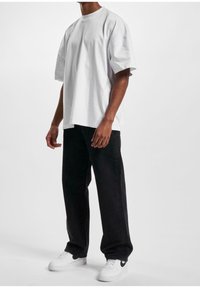 T-shirt bianca in cotone con maniche corte, abbinata a jeans neri a gamba dritta. Indossata con sneakers bianche con accenti neri.