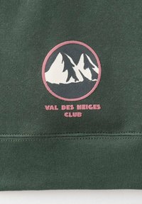 Zelená mikina s obľúbenou kruhovou nálepkou, na ktorej sú čierne a biele siluety hôr, obklopené ružovým okrajom, a nápisom "VAL DES NEIGES CLUB" nižšie.