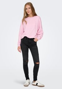 Sudadera rosa con el texto "PARIS", jeans skinny negros rasgados y zapatillas blancas con detalles en negro. Conjunto casual con corte relajado.