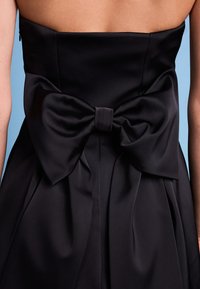 Schwarzes trägerloses Kleid mit einer großen, satinierten Schleife auf der Rückseite, mit glatter Textur und gefälteltem Rockdetail.