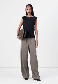 Top sem mangas em malha canelada azul marinho com um design em forma de V, combinado com calças largas cinza claro. Modelo segura uma clutch texturizada em castanho.