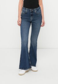 Τζιν παντελόνια με καμπάνα σε σκούρο μπλε, με κλασικό σχέδιο πέντε τσεπών και ελαφρώς φθαρμένο στρίφωμα. Κατασκευασμένα από βαμβάκι με ομαλή υφή.